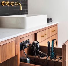 a bathroom with a sink and some hair dryers in the drawer under the faucet