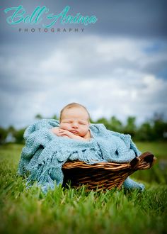 a baby wrapped in a blue blanket is laying in a wicker basket on the grass