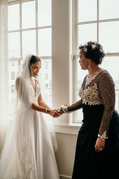 two women standing next to each other in front of a window with one holding the bride's hand