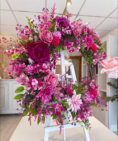 a floral wreath is displayed on a easel in a room with pink and purple flowers