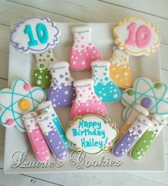 a birthday cake decorated with colorful science themed cookies on a white platter that says happy birthday haley