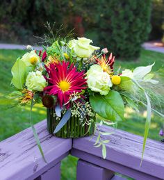 a bouquet of flowers sitting on top of a purple bench in front of some grass