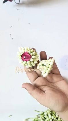 a person's hand holding two small flowers in their left hand, and another flower on the right