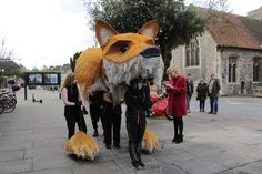 two women are standing next to a large stuffed fox on the sidewalk in front of a building