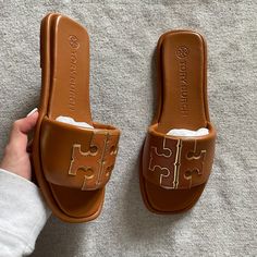 "The Sport Slide Is Made Of Soft Padded Leather That Hugs The Foot, With A Cushioned Foam Insole For Flexible Support. The Raised Double T Is Edged In Metallic Trim For Subtle Shine." Preowned, Only Worn Once - Size 7 - Color: Bourbon Miele / Gold - Comes With Box, Original Packaging, & Dustbag - Padded Napa Leather Upper - Metallic Calfskin Trim - Cushioned Insole Will Trade For The Cream Or Black Ones Tory Burch Slippers, Black Wedge Flip Flops, Tory Burch Slides, Tory Burch Sandal, Tan Leather Sandals, Pretty Sandals, Pretty Shoes Sneakers, Fashion Shoes Heels, Leather Footwear