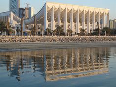 a large white building sitting next to a body of water with palm trees in front of it