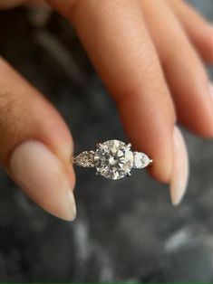 a woman's hand holding an engagement ring with three stones on the top and bottom