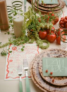 the table is set with plates, silverware and tomatoes