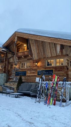 skis are lined up in front of a wooden building with snow on the ground