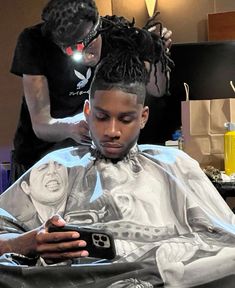 a man getting his hair cut while another person looks at the phone in front of him