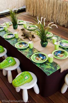 a table set with plates, cups and plants on it for a children's birthday party