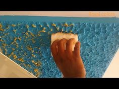 a person using a sponge to paint a blue and yellow wall with gold flecks