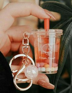 a person holding a cup with a keychain attached to it and a drink in the other hand