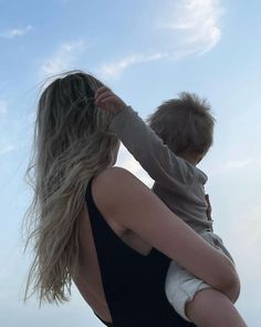 a woman holding a child in her arms while standing on top of a sandy beach