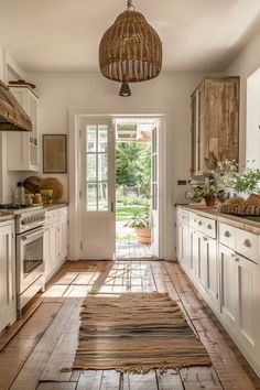 a kitchen with wooden floors and white cabinets, an open door leading to the outside