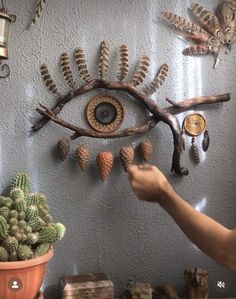 a person pointing at an eye made out of branches and pine cones on a wall