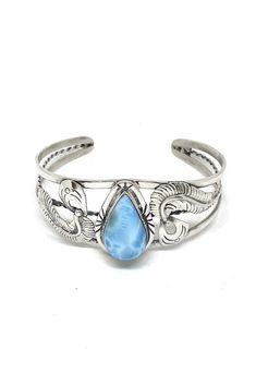 This Navajo handmade sterling silver cuff bracelet features a beautiful teardrop genuine Larimar stone. The artist added handmade sterling silver feathers on each side of the stone and added hand stamped details. Larimar is a rare stone mined only in the Dominican Republic where it was thought to be from the Lost City of Atlantis. It actually comes from a volcanic deposit on the island. The discoverer of this stone named it for his daughter, Larissa, and mar meaning sea in Spanish. The soft blue Feather Cuff, Larimar Jewelry, Silver Eagle, Larimar Stone, Rare Stone, Silver Eagles, American Turquoise, The Dominican Republic, Silver Feather