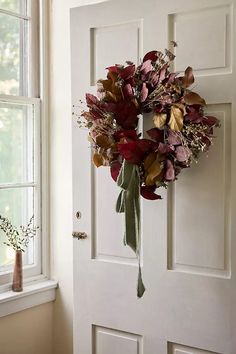 a wreath hanging on the front door of a house with leaves and flowers in it