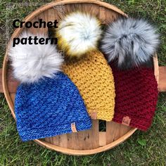 three knitted hats with pom - poms on top of a wooden basket