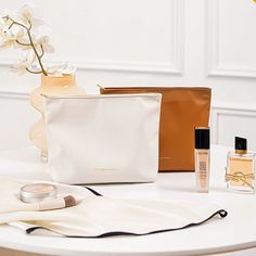 the contents of a purse and cosmetics bag on a white table with flowers in it