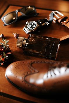 an assortment of men's accessories on top of a wooden table next to a pair of sunglasses