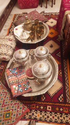 two trays with silver dishes on them sitting on top of a colorful area rug