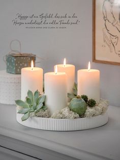 three white candles with succulents and greenery sit on a round tray