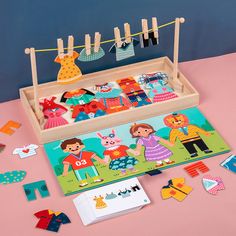 children's wooden clothes pegs in a box on a pink surface next to cards and magnets