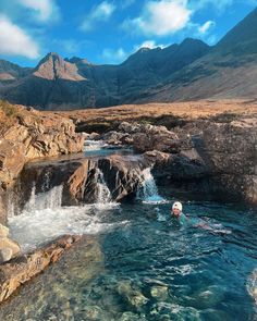 a person swimming in a pool with mountains in the background and blue water running through it