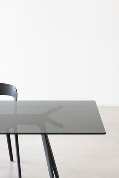 a glass table with a black chair and white wall in the backgrounnd