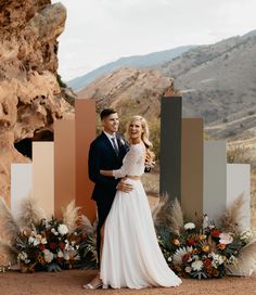 a man and woman standing next to each other in front of an arch with flowers