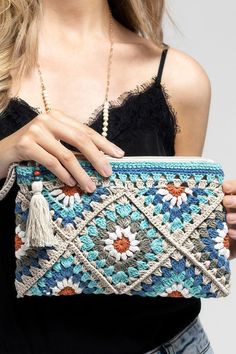 a woman holding a crocheted purse with tassels and beads on it