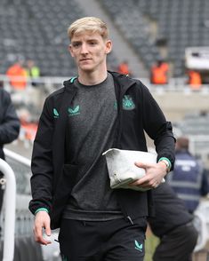 a man in black jacket and shorts holding a white bag on top of a field