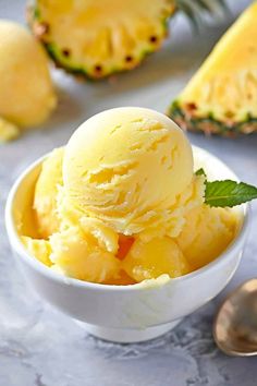 a white bowl filled with ice cream next to two pieces of pineapple on a table