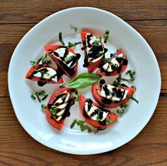 a white plate topped with sliced tomatoes covered in black and white sauce on top of a wooden table