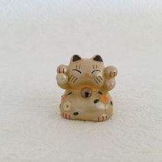 a ceramic cat figurine sitting on top of a white surface with its eyes closed