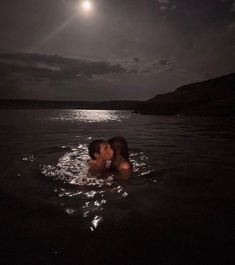 two people are kissing in the water at night with the moon above them and dark clouds