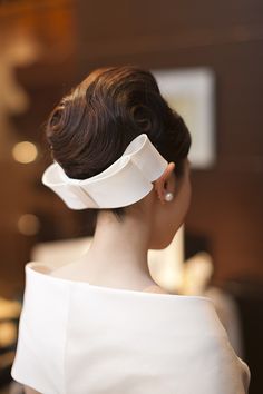 a woman in a white dress with a large hair piece on her head, looking off to the side