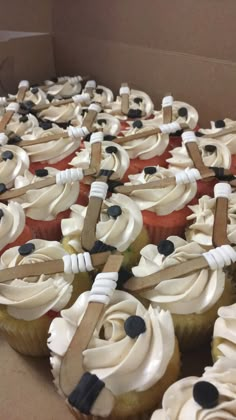 cupcakes with white frosting and black piping are arranged in a box