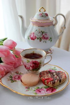 a tea pot with pink flowers next to a cup and saucer on a plate