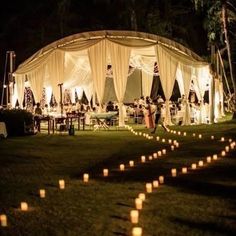 an outdoor tent with candles in the grass and people standing around it at night time