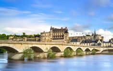 an old bridge crosses over the water in front of a castle like building with spires