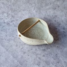 a ceramic bowl with a wooden stick sticking out of the top, on a concrete floor