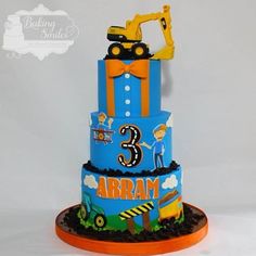 a three tiered blue cake with construction vehicles on top and an orange ribbon around the bottom