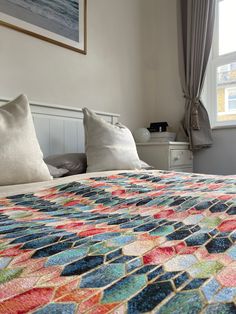 a bed with a colorful quilt on top of it next to two pillows and a window