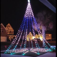 a lighted christmas tree in the middle of a street with palm trees and houses behind it