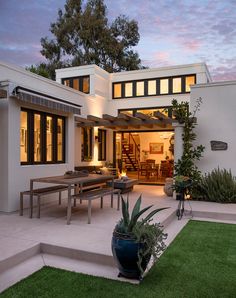 a modern house with an outdoor patio and dining area in the back yard at dusk