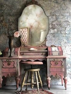 an antique vanity with mirror and stools in front of brick wall, decorated with flowers