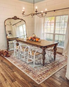 a dining room table with white chairs and a dog laying on the floor in front of it