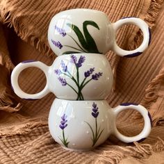 three coffee mugs are stacked on top of each other with purple flowers painted on them